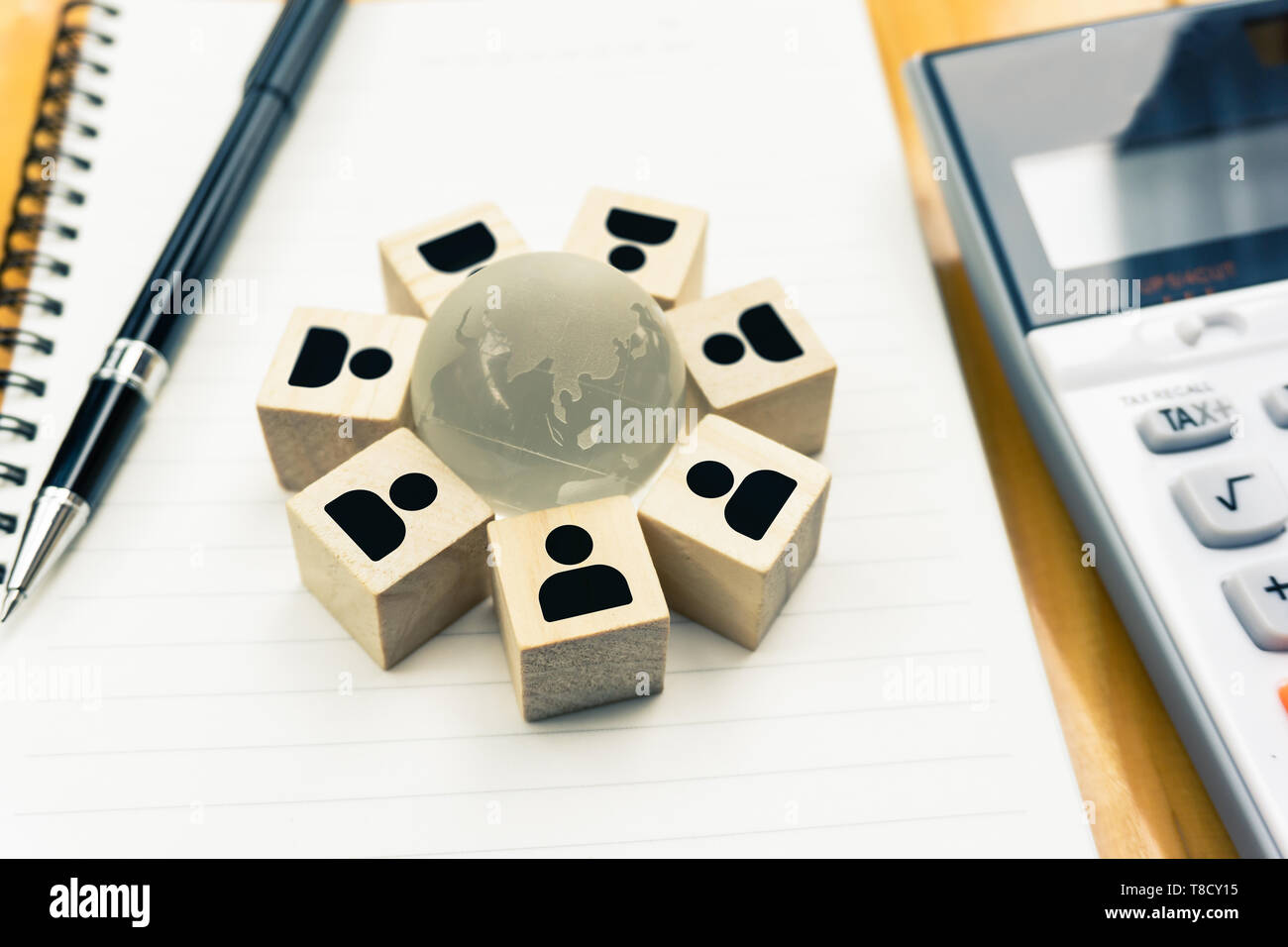 Global Business network concepts. A businessman icon wooden blocks stand around the globe crystal on notebook with black pen and calculator. Depicts a Stock Photo