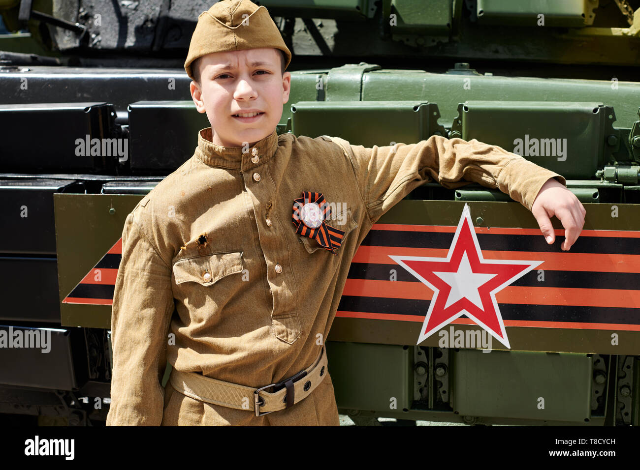 Boy dressed in Soviet military uniform during the second world war posing near army tank Stock Photo