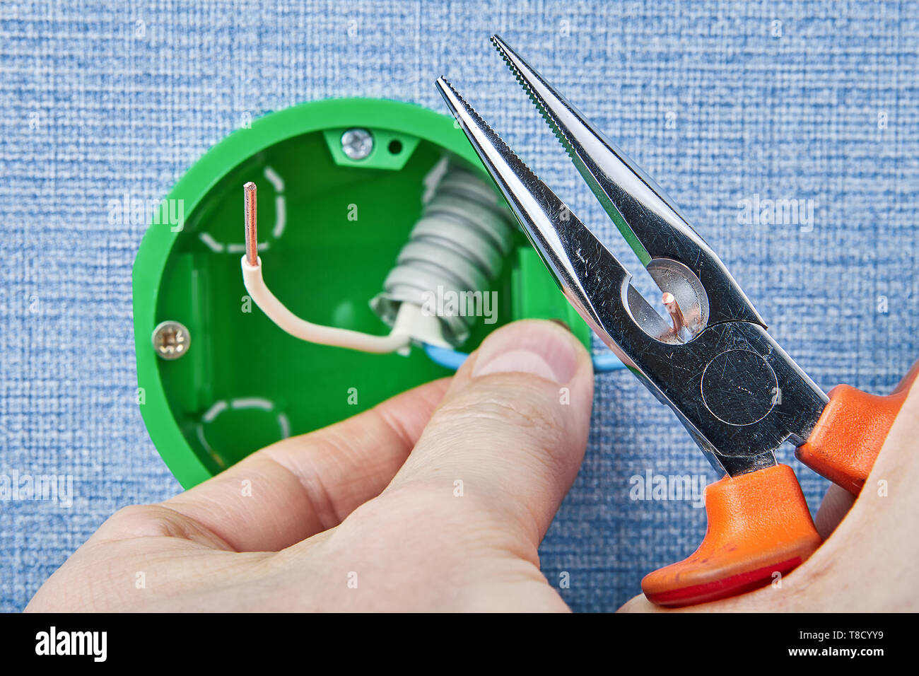 Repairman is installing new round electrical box cutting copper wiring with long nose pliers, electric installation work. Stock Photo