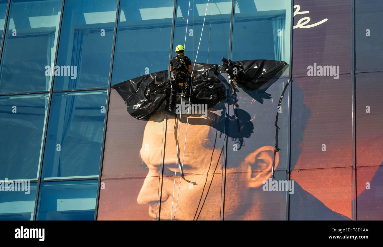 CANNES, FRANCE - APRIL 2019: Specialist maintenance operative abseiling down the side of the Palais des Festivals in Cannes to remove plastic advertis Stock Photo