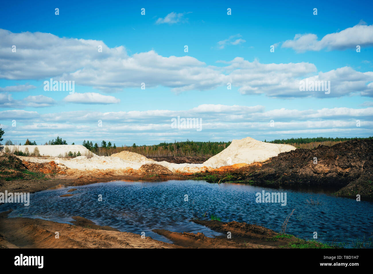 Industrial sand quarry with artificial reservoir. Sand pit. Construction industry. Sand hills agains the blue sky. Stock Photo