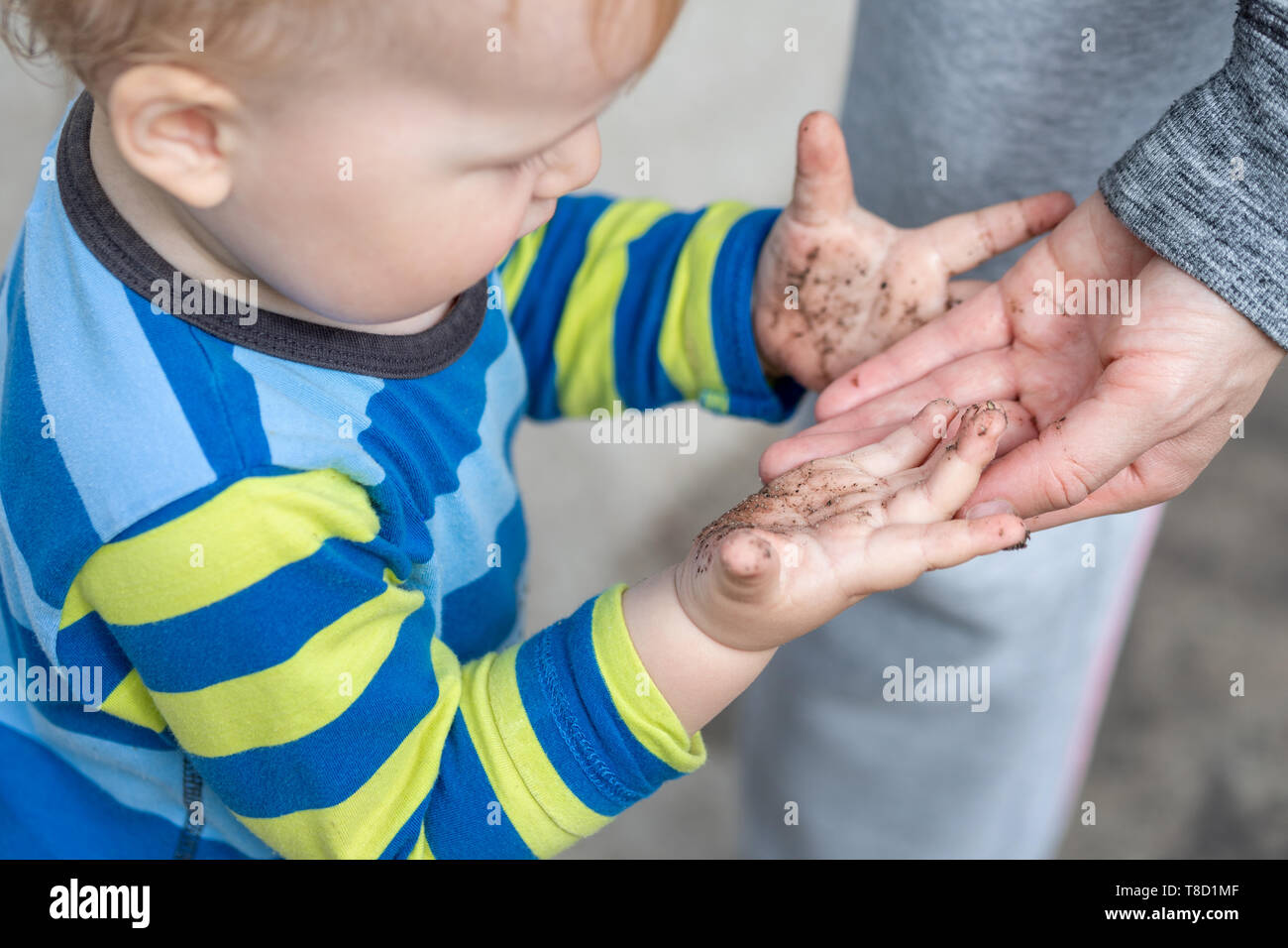Cute little toddler boy showing mother dirty hands after playing in mud