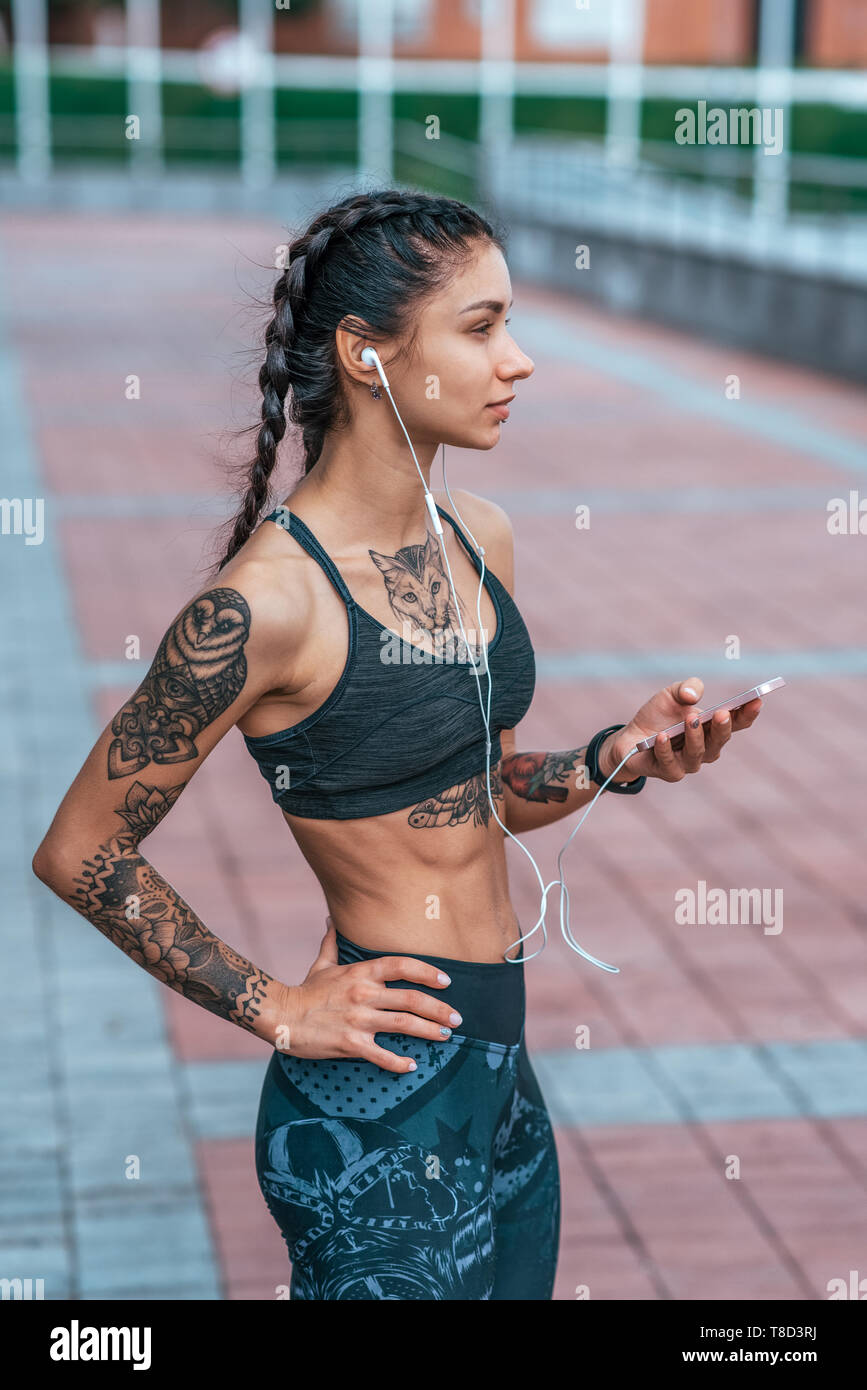 A beautiful girl is an athlete with tanned skin and cat tattoos. Happy  smiles. Emotionally and confidently looks into frame. The concept of  strength and confidence. In sportswear hair in braids Stock