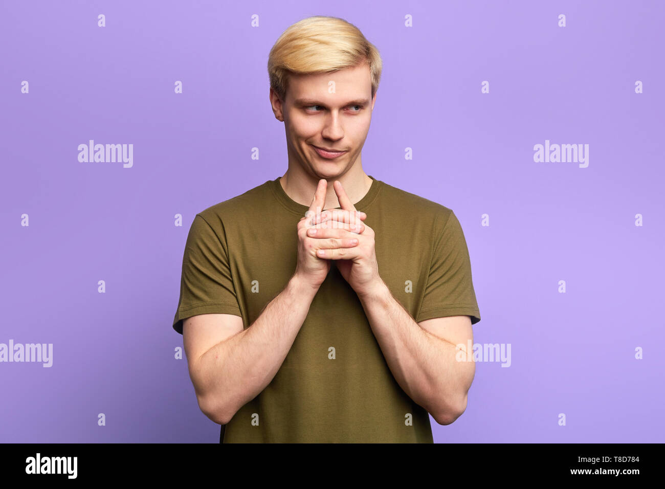 Sly cunning playful man touching chin with finger and looking away, making up a plan, isolated over violet background Stock Photo