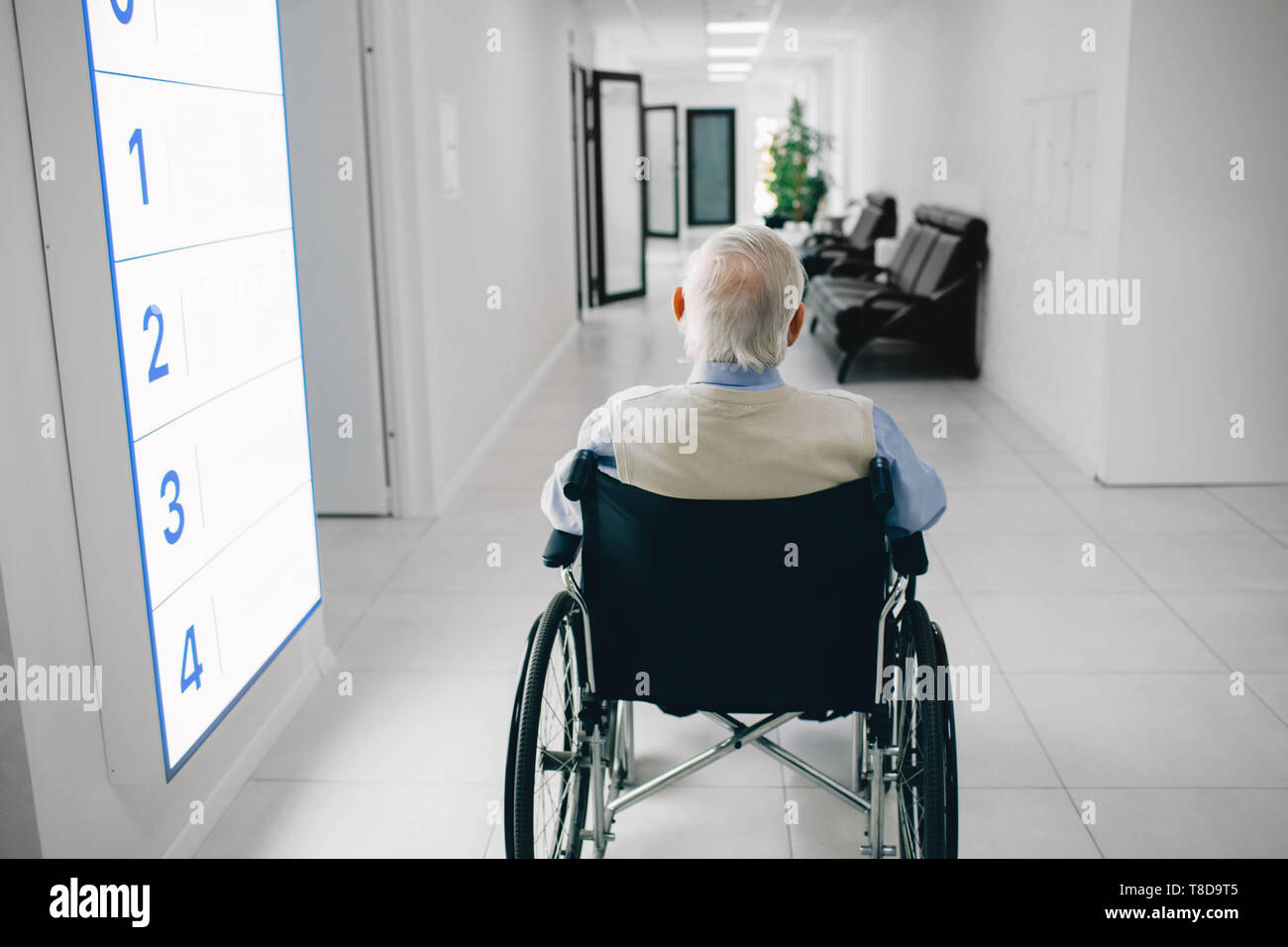 Lonely senior man in wheelchair sitting at the hospital corridor, back view. Stock Photo