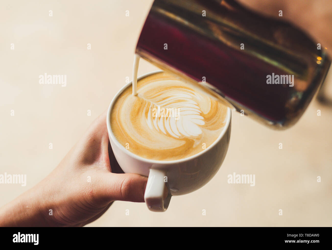 Closeup image of female barista holding and pouring milk for prepare cup of coffee, latte art, vintage color tone, coffee preparation and service conc Stock Photo