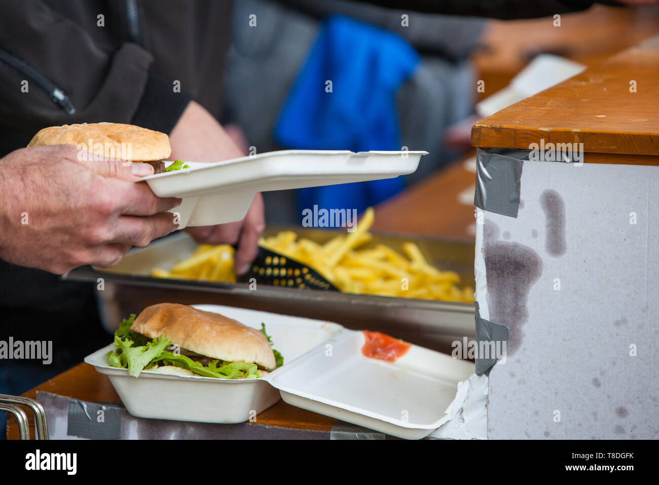 Preparing take away meal with freshly cooked burger and french fries on outdoors kitchen at street music festival in Gland, Vaud, Switzerland Stock Photo