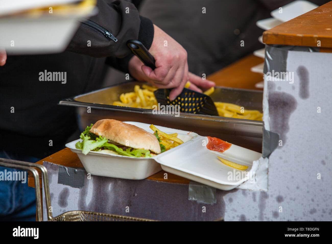 Preparing take away meal portion with freshly cooked burger and french fries on outdoors kitchen at street music festival in Gland, Vaud, Switzerland Stock Photo