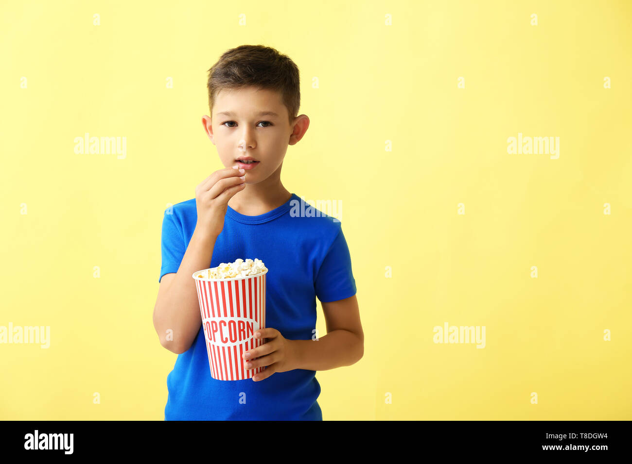 Cute little boy eating popcorn on color background Stock Photo Alamy