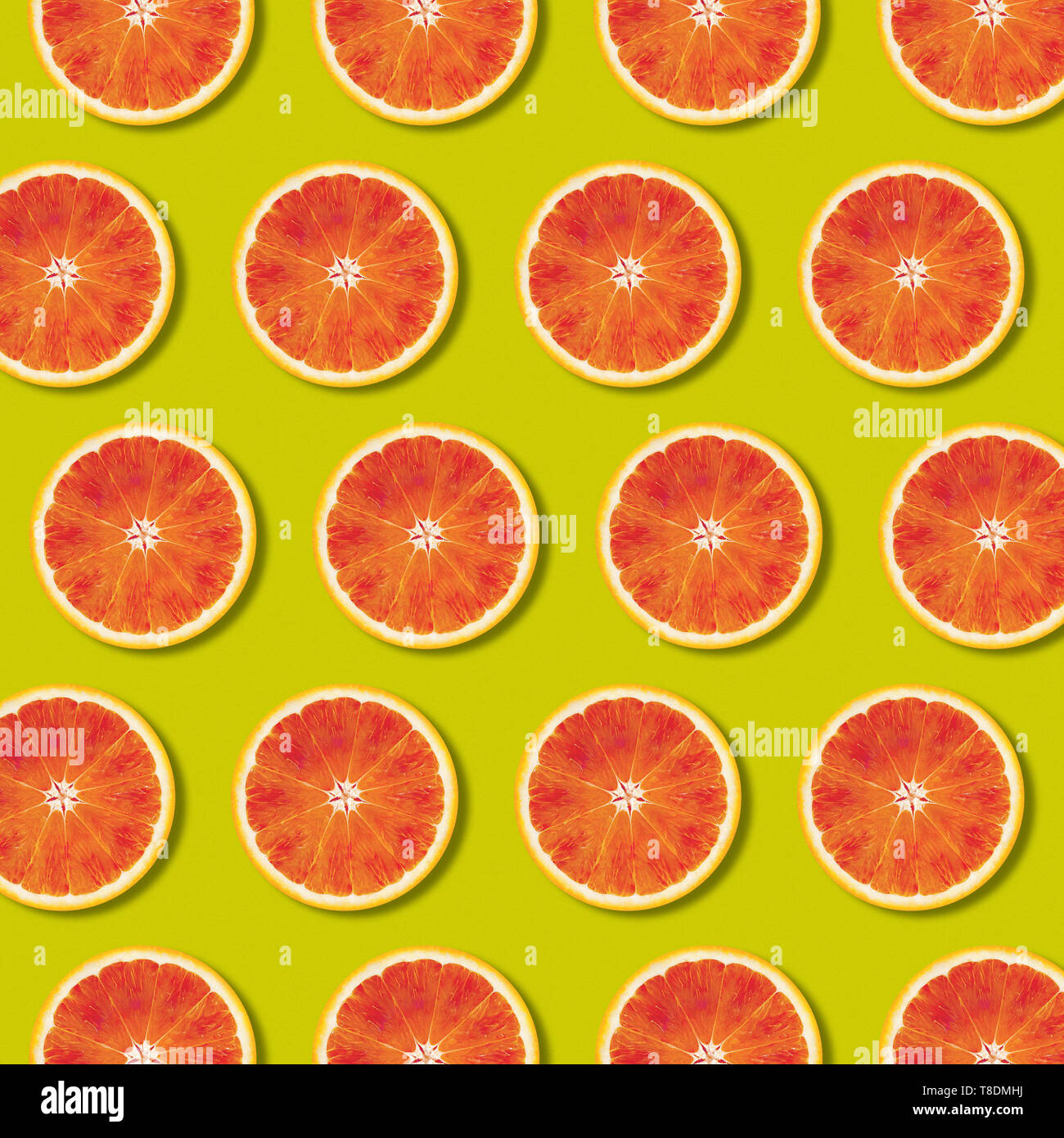 Geometric red orange fruit slices pattern on green color background. Minimal flat lay, top view food texture Stock Photo