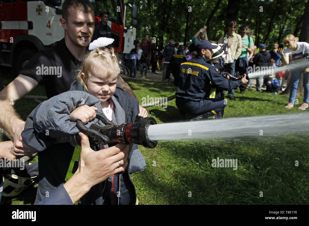 Kiev, Ukraine. 12th May, 2019. A little girl pours water from fire hose during 'City of professions' children's festival in Kiev, Ukraine, on 12 May 2019. The City of Professions is a children's career-oriented festival whose goal is to provide children to try themselves in different professions - rescuers, firemen, bomb experts, policemen, doctors, social workers, criminologists, aircraft designer, atomic engineer, a businessman, a scientist, and others. Credit: Serg Glovny/ZUMA Wire/Alamy Live News Stock Photo