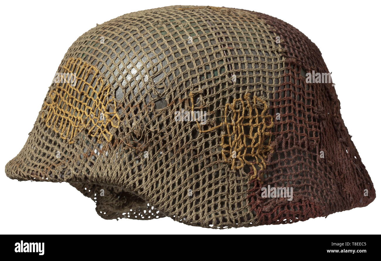 A helmet M 35 with camouflage Field-applied camouflage paint in different shades of green, over which is a simple wire covering for attachment of camouflage material, as well as a British camo net. The inside with the original field-grey paint and laterally struck stamping 'ET 68', M 1931 interior fittings. Chin strap missing. In undisturbed, as found condition. The shortage of camouflage covering was made up for in Army units by simple provisional paint of all types. The large quantities of captured equipment available at the invasion front or at the Arnheim Bridge were en, Editorial-Use-Only Stock Photo
