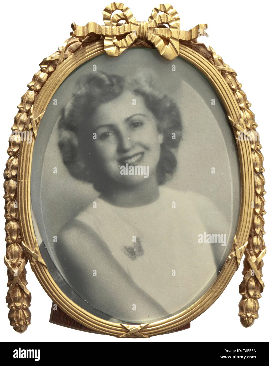 Eva Braun (1912 - 1945) - a portrait photo in a gold empire frame Portrait of young Eva Braun with butterfly brooch, the photo is a reproduction commissioned by Evas´s sister Ilse. The gold empire frame made by the Aachen jeweller Heinrich Steenaerts, hallmark '585', jeweller´s signature, height of frame 90 mm, 45.5 g. The back of the photo with handwritten note (tr) 'Hitler´s favourite photo of Eva. Reproduction developed after the war from an original negative. The frame comes from Hitler´s or Eva Braun´s possessions.' Heinrich Steenaerts, royal imperial court jeweller, g, Editorial-Use-Only Stock Photo