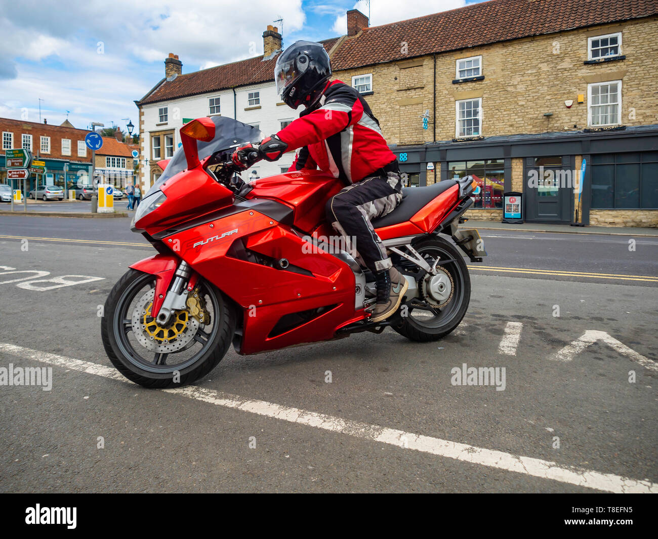 A motor cyclist riding a red Aprilia Futura Motor cycle pulling up at a Favorite stopping place in Helmsley Market North Yorkshire Stock Photo