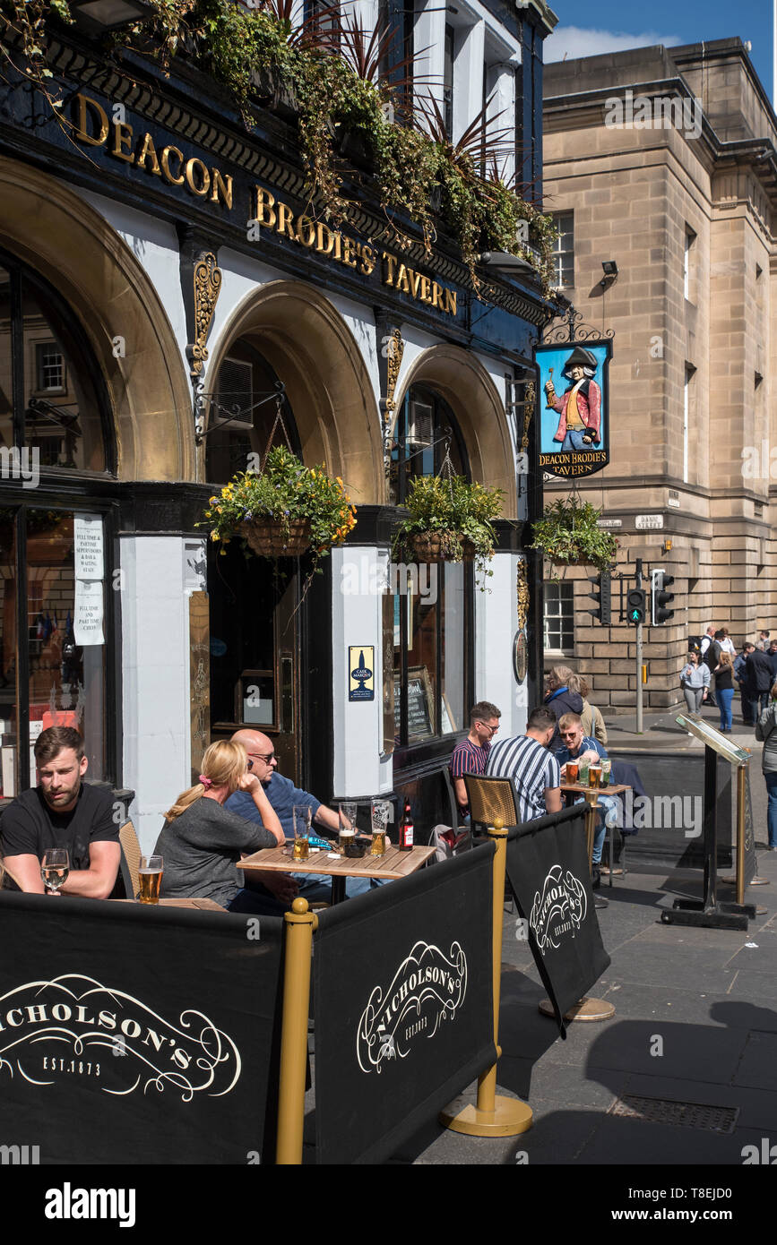 Customers enjoying a drink in the sunshine outside Deacon Brodie's Tavern in the Lawnmarket, Edinburgh, Scotland, UK. Stock Photo