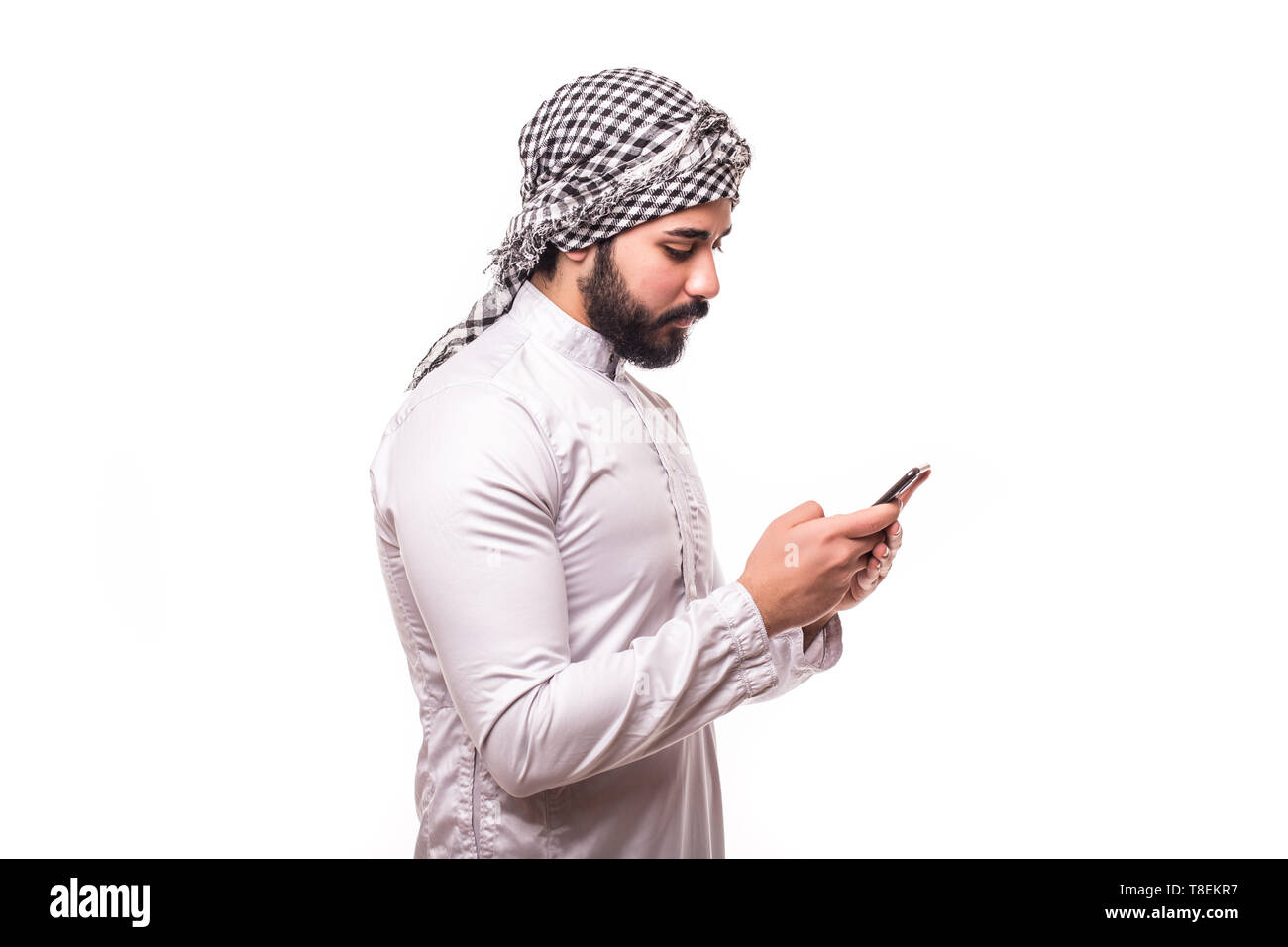 Young arab man wearing in traditional abaya clothes with phone on white background Stock Photo