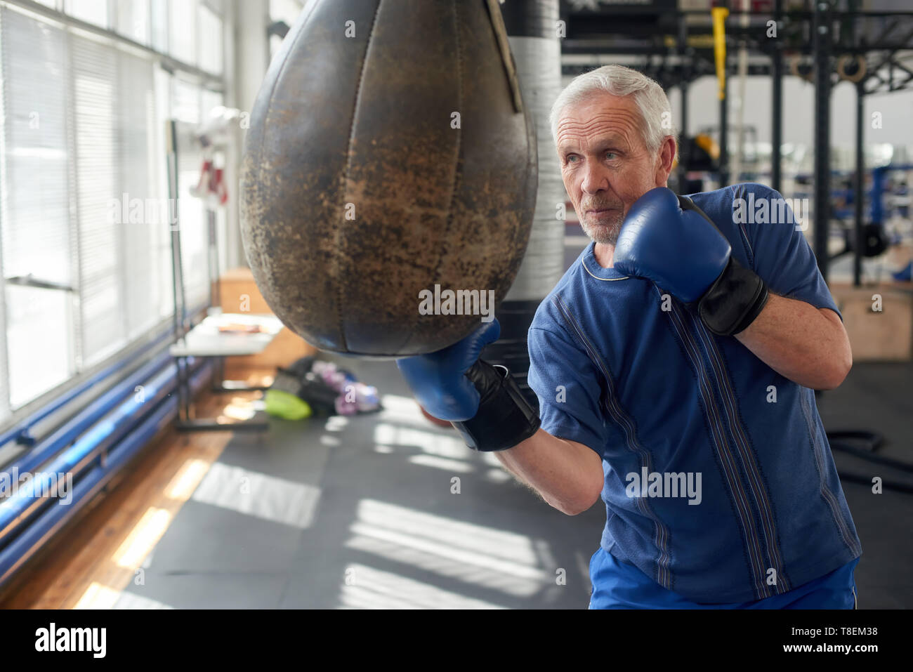 Elderly man hitting punching bag in boxing studio. Senior caucasian man