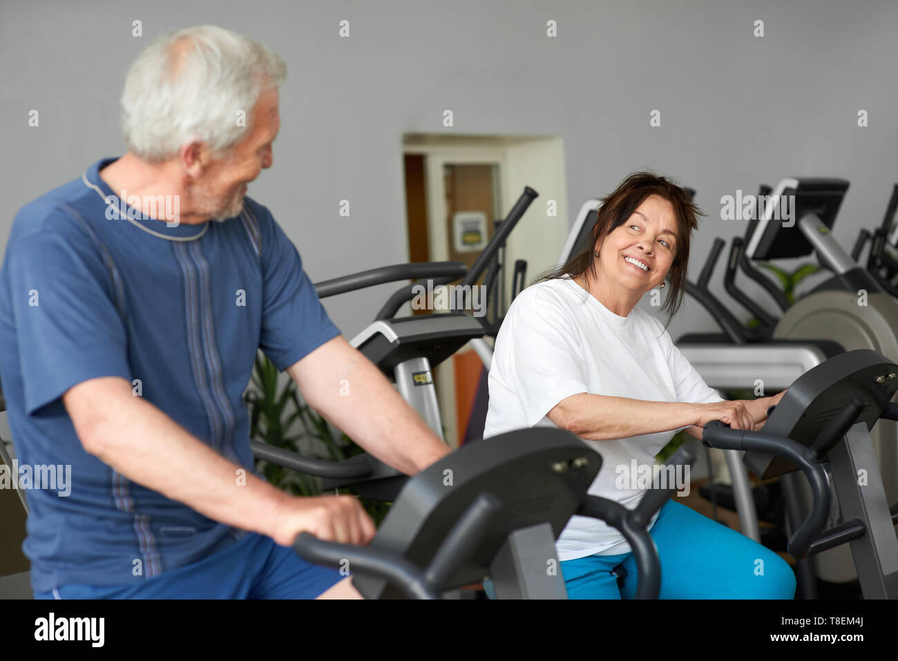 Beautiful couple of seniors working out at gym. Elderly man and woman  training on machine at fitness club, focus on woman. Aged people doing  cardio wo Stock Photo - Alamy