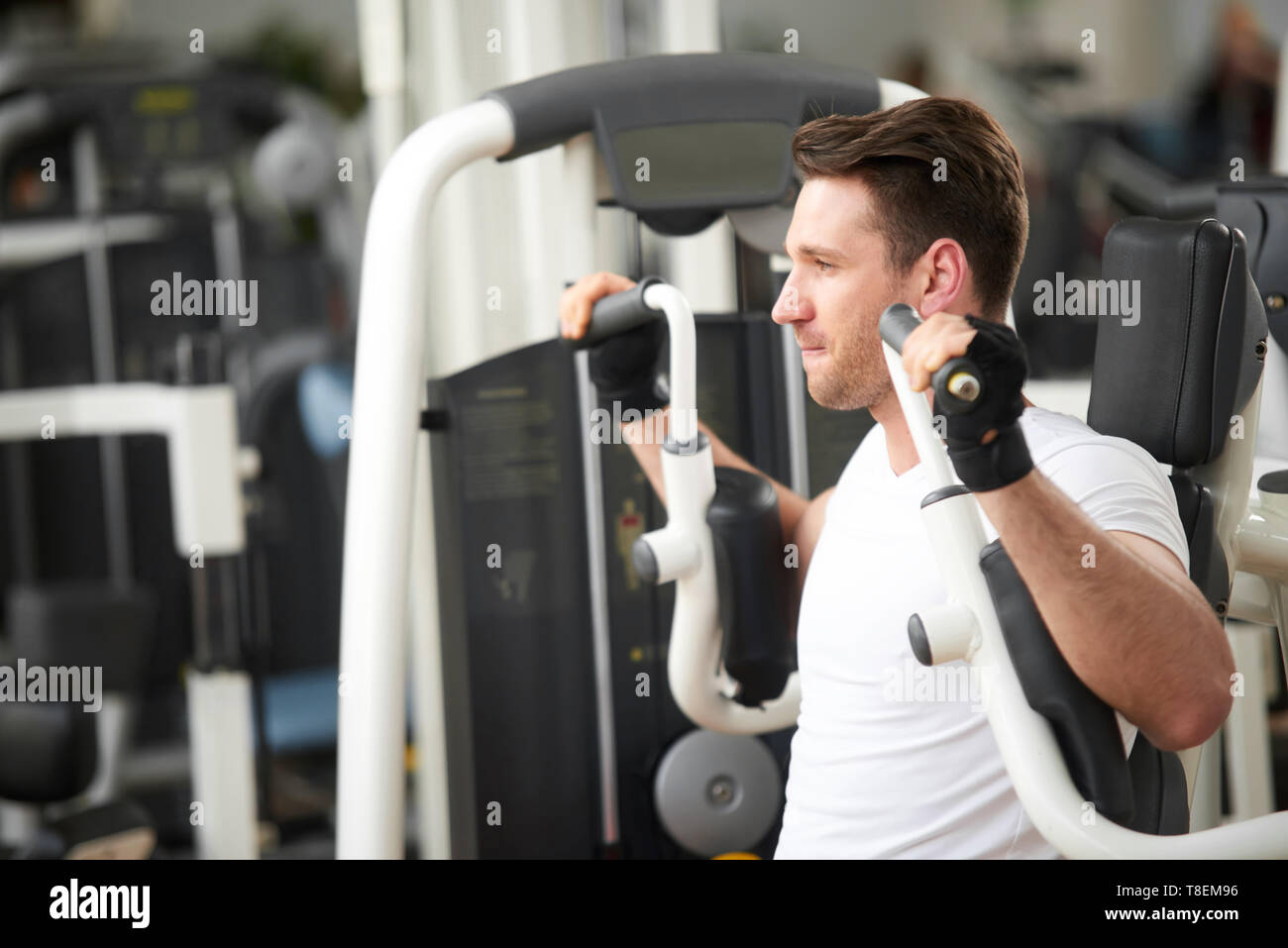 Young athletic man working out in gym. Fitness athlete doing chest exercises on press machine. People, sport, active livestyle. Stock Photo