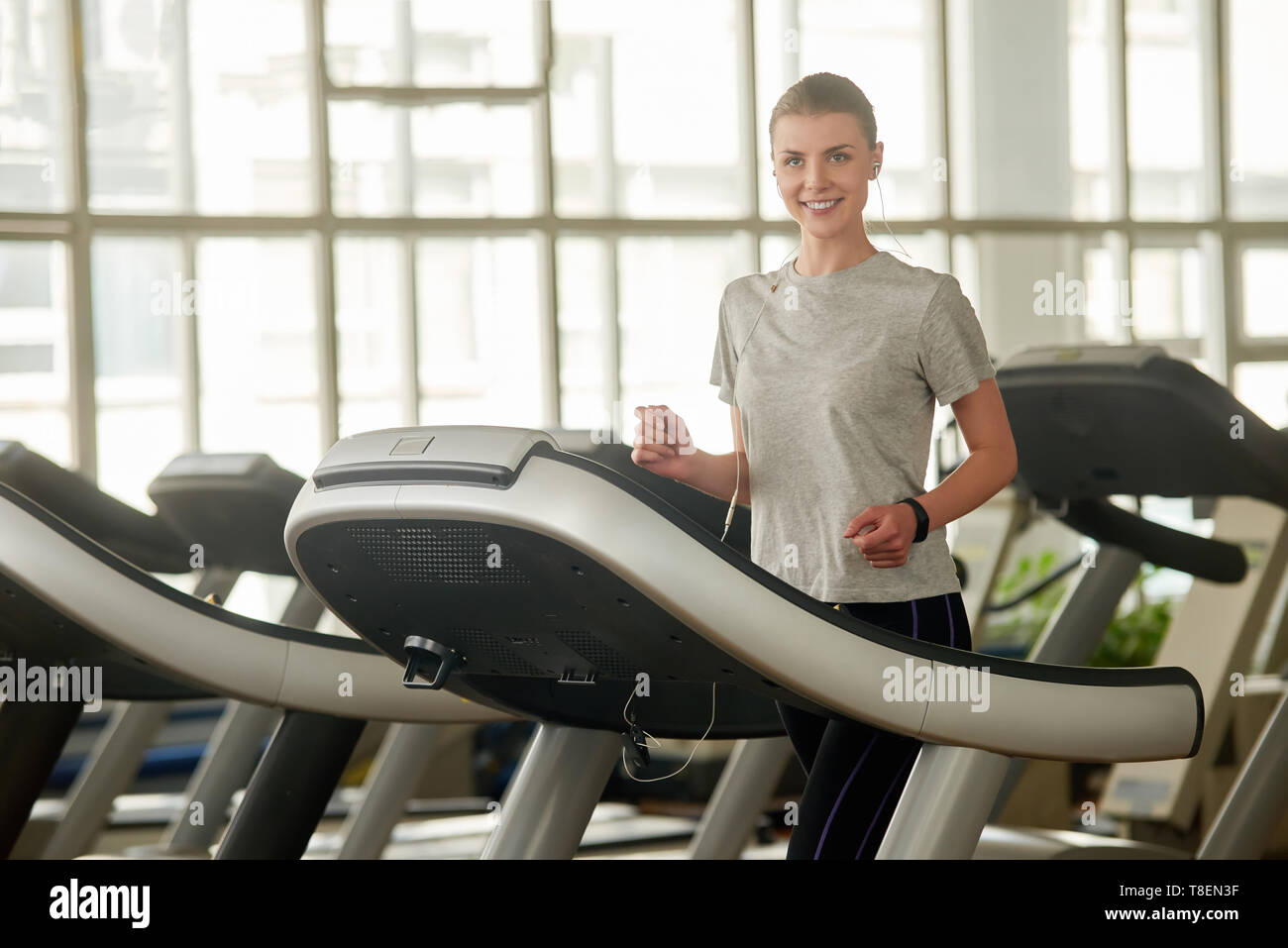 Pretty smiling woman on treadmill at gym. Portrait of happy girl in earphones working out at modern gym. Concept of morning workout Stock Photo Alamy