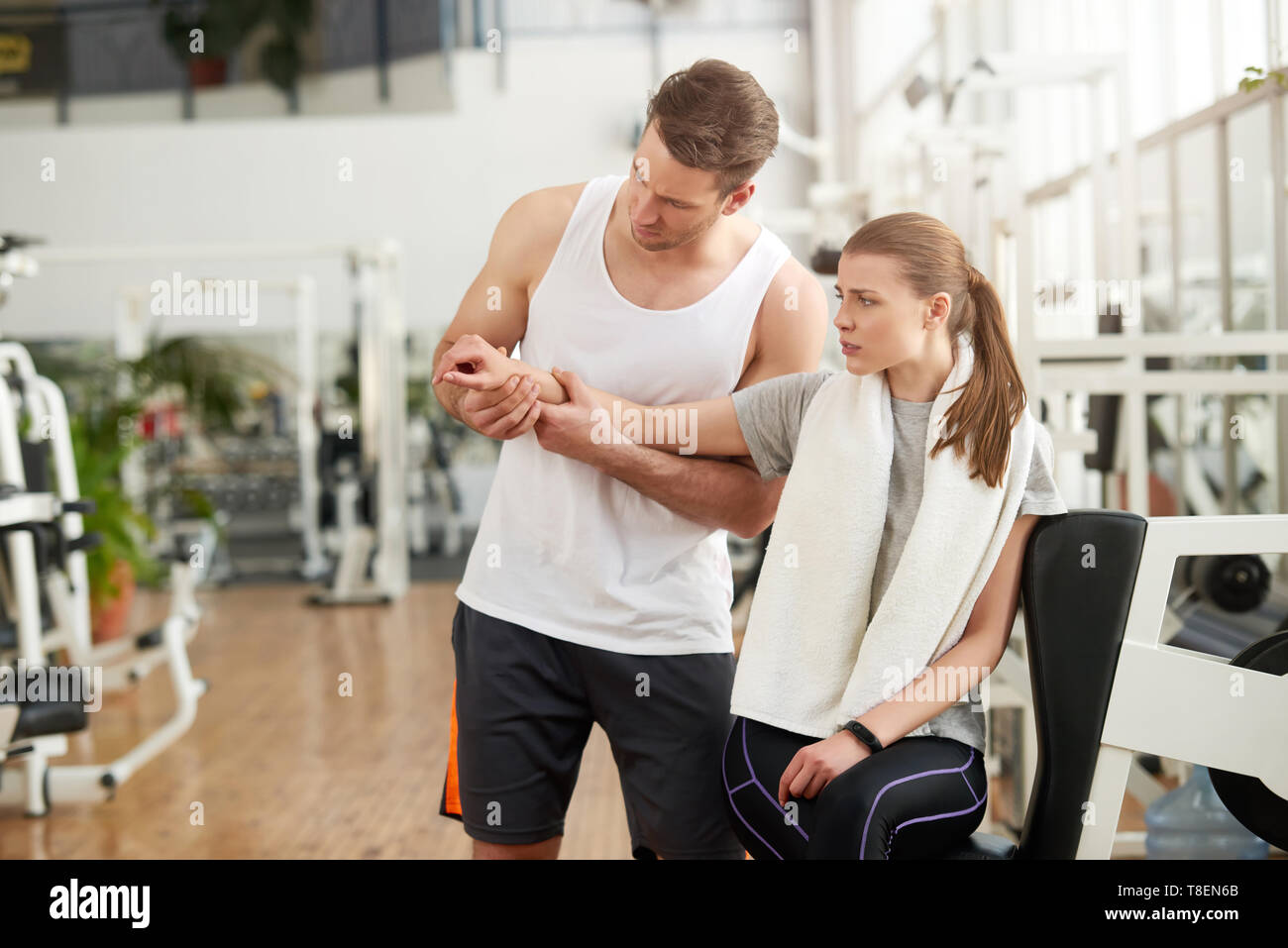 Woman with joint pain in gym. Young muscular trainer touching female