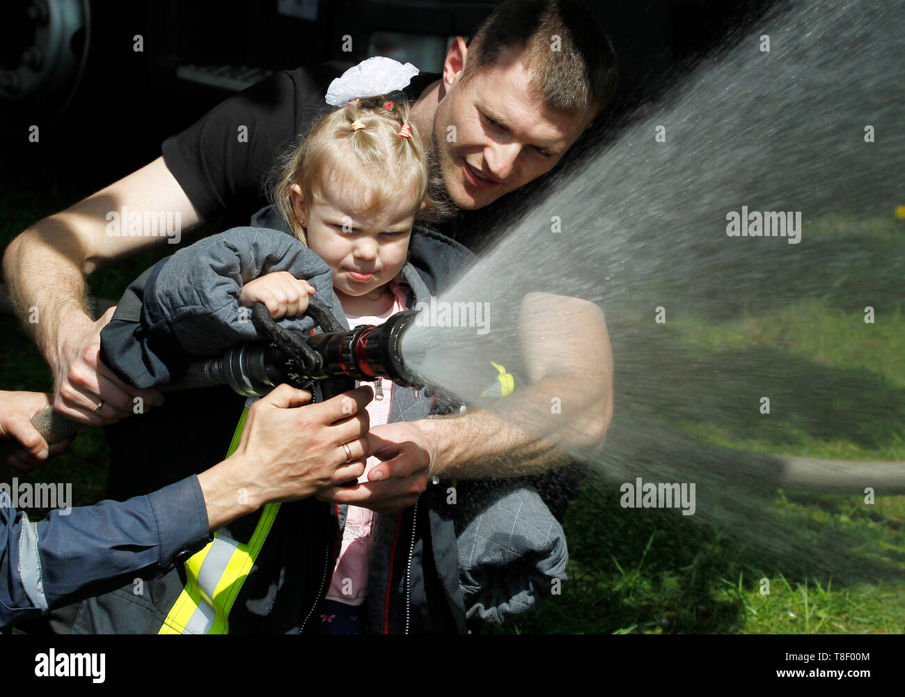 Ukrainian little girl seen pouring water from a fire hose during the festival. Children festival also called City of professions. The festival is a children's career-oriented festival exposing them to different professions like atomic engineer, businessmen, scientist, rescuers, bomb experts, policemen, doctors, social workers, criminologists, aircraft designer, firemen and other professions. Stock Photo