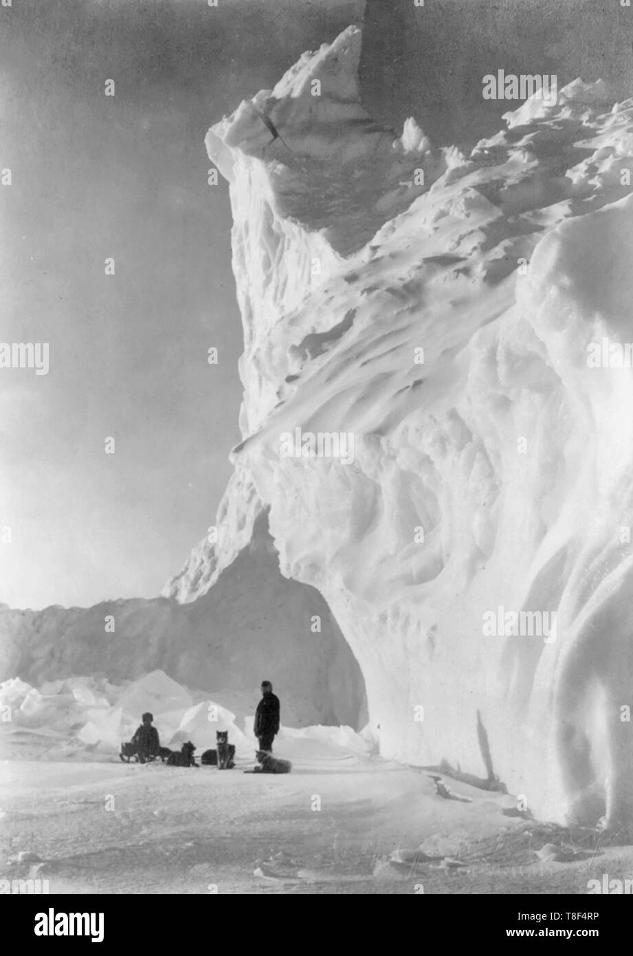 Dog team resting by an iceberg - Photograph shows two men resting with a dogsled team near an iceberg, during the British Antarctic Expedition, circa 1910 Stock Photo