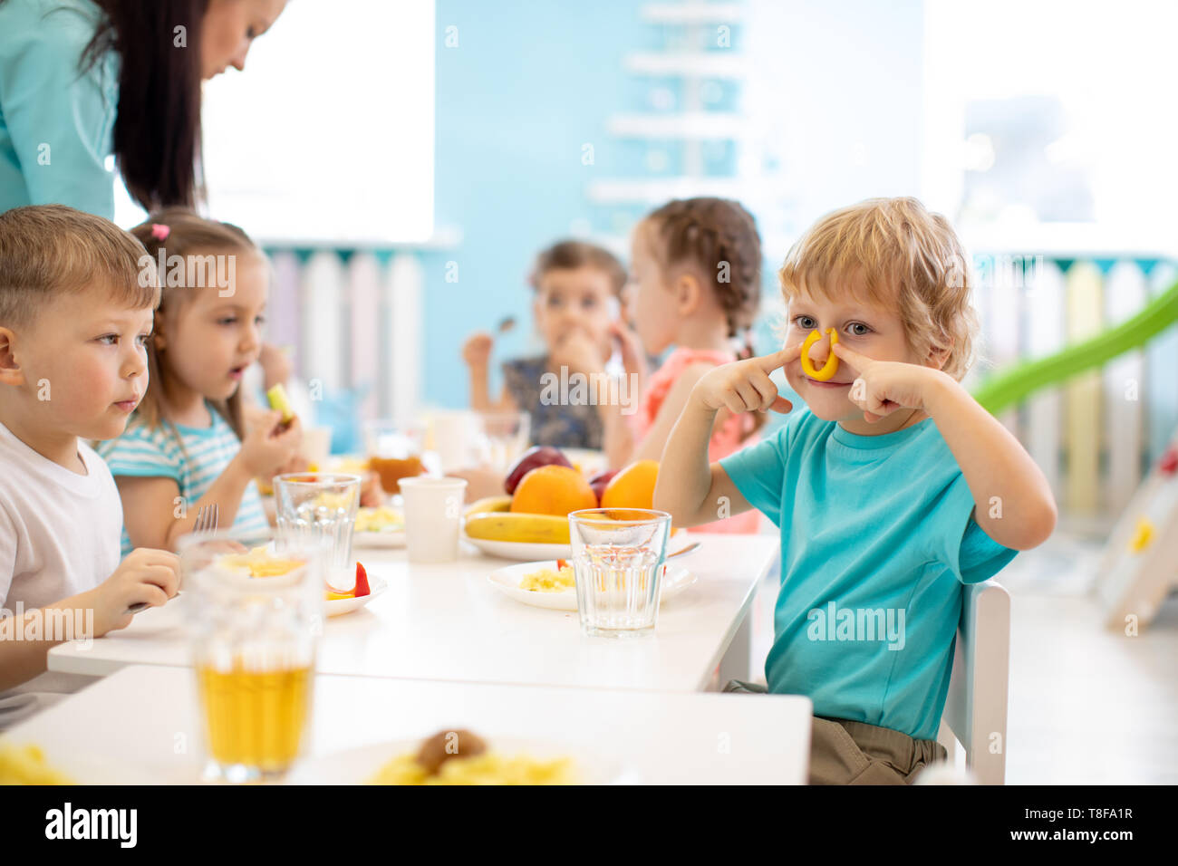 Group of kids have lunch in daycare. Child boy dabbles at the table