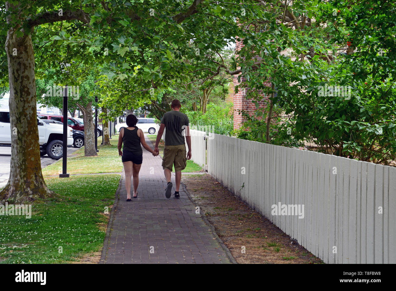 A couple walks down a tree shaded sidewalk near downtown in the