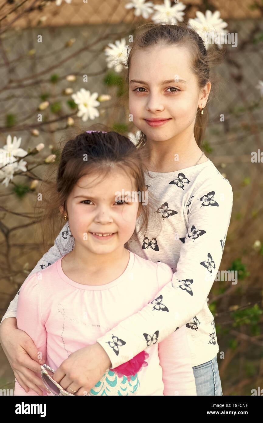 Little girls pose on floral blossom in spring garden. Sisters enjoy spring day outdoor. Children with blossoming flowers. Family, love and trust concept. Stock Photo
