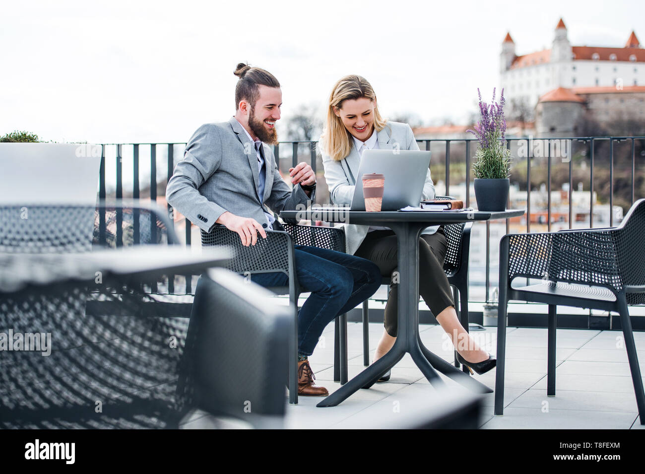 Two young business people with laptop sitting on a terrace outside office, working. Stock Photo