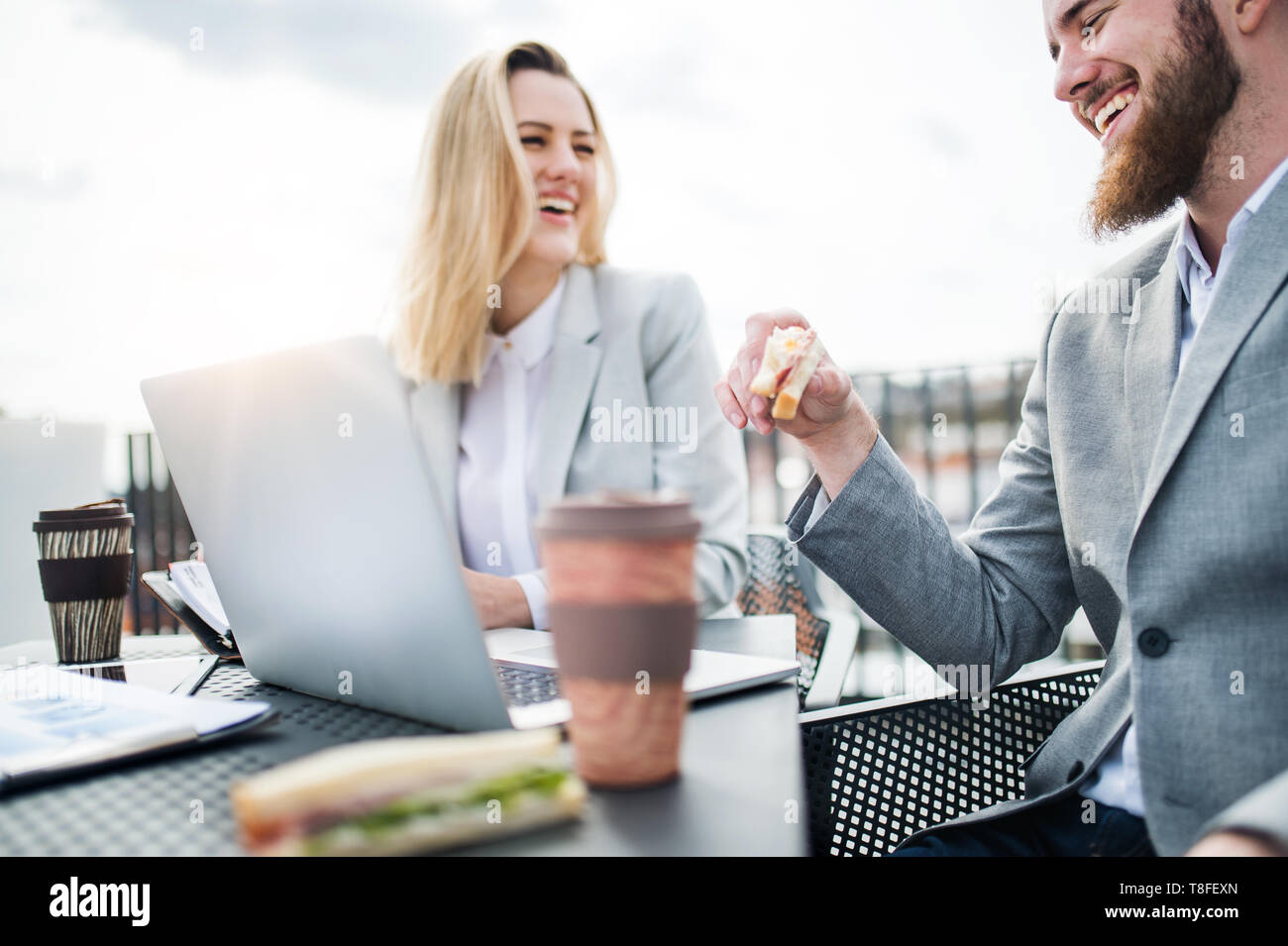 Businesspeople with laptop sitting on a terrace outside office, working and eating. Stock Photo