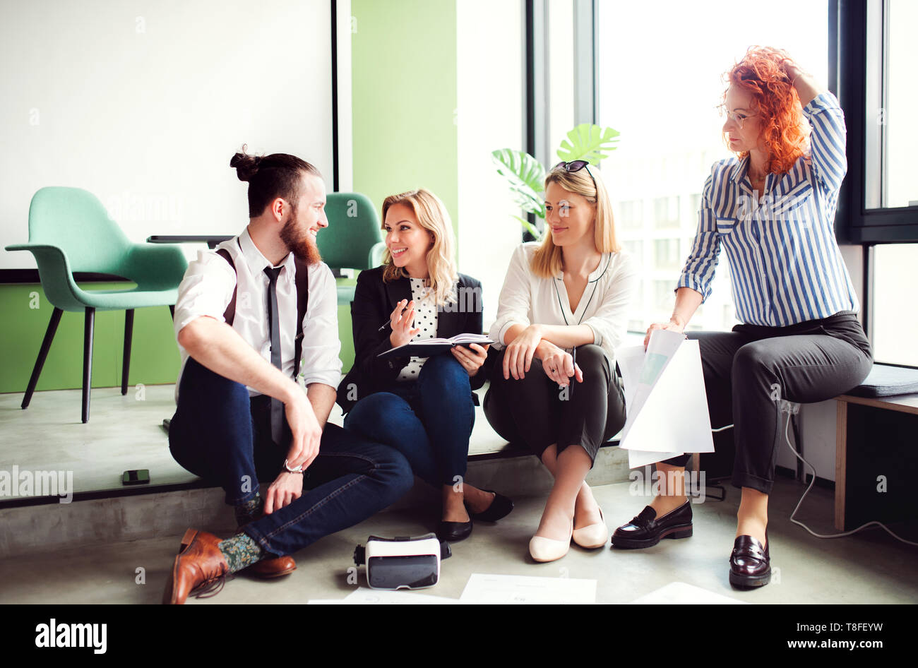 A group of young business people sitting on the floor in an office, talking. Stock Photo