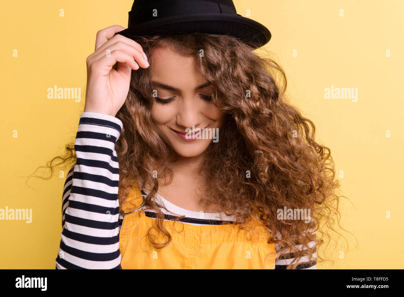 Portrait of a young woman with black hat in a studio on a yellow background. Stock Photo
