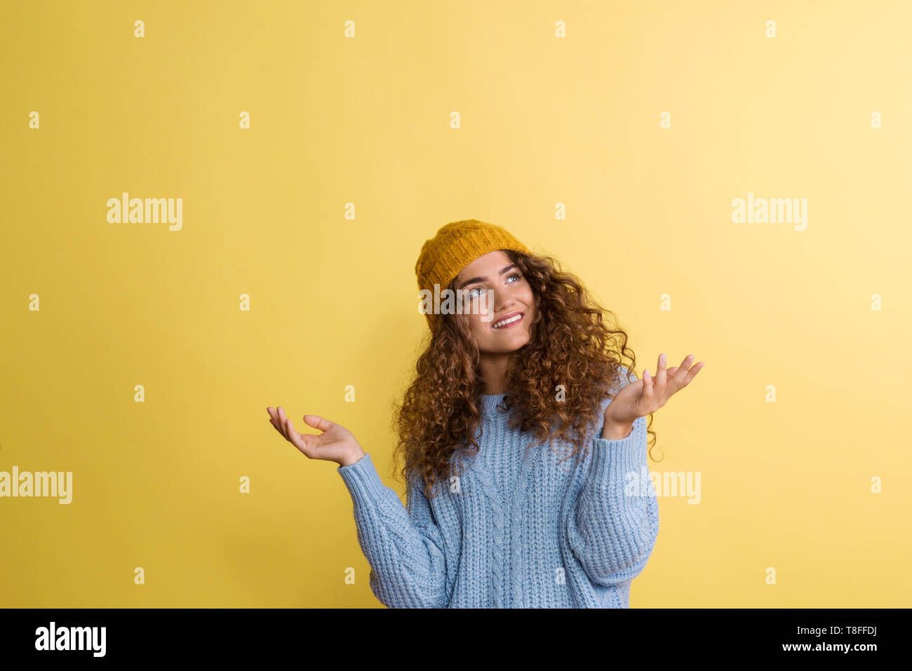 Portrait of a young woman with woolen hat in a studio on a yellow background. Stock Photo