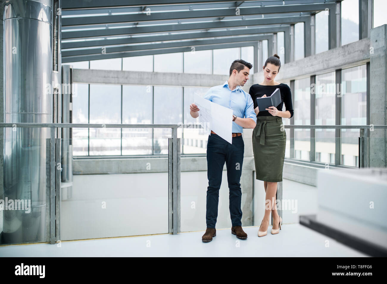 Two young architects with blueprints standing in office, talking. Stock Photo