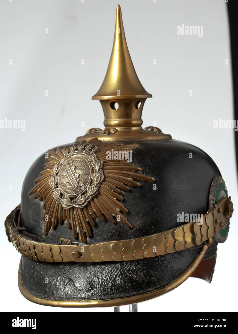 A helmet for a one-year volunteer of the infantry, circa 1900 Black painted leather skull (with craquelures) with gilt brass fittings, yellow rayed emblem with applied nickel silver coat of arms, the circular base with stars and unscrewable spike. Flat brass chinscales with leather underlay on button 91, imperial and state cockades. Brown silk rep liner and brown leather sweatband. Signs of usage and age. A beautiful, untouched piece. historic, historical, Saxony, Saxonia, Saxonian, German, Germany, 20th century, Additional-Rights-Clearance-Info-Not-Available Stock Photo