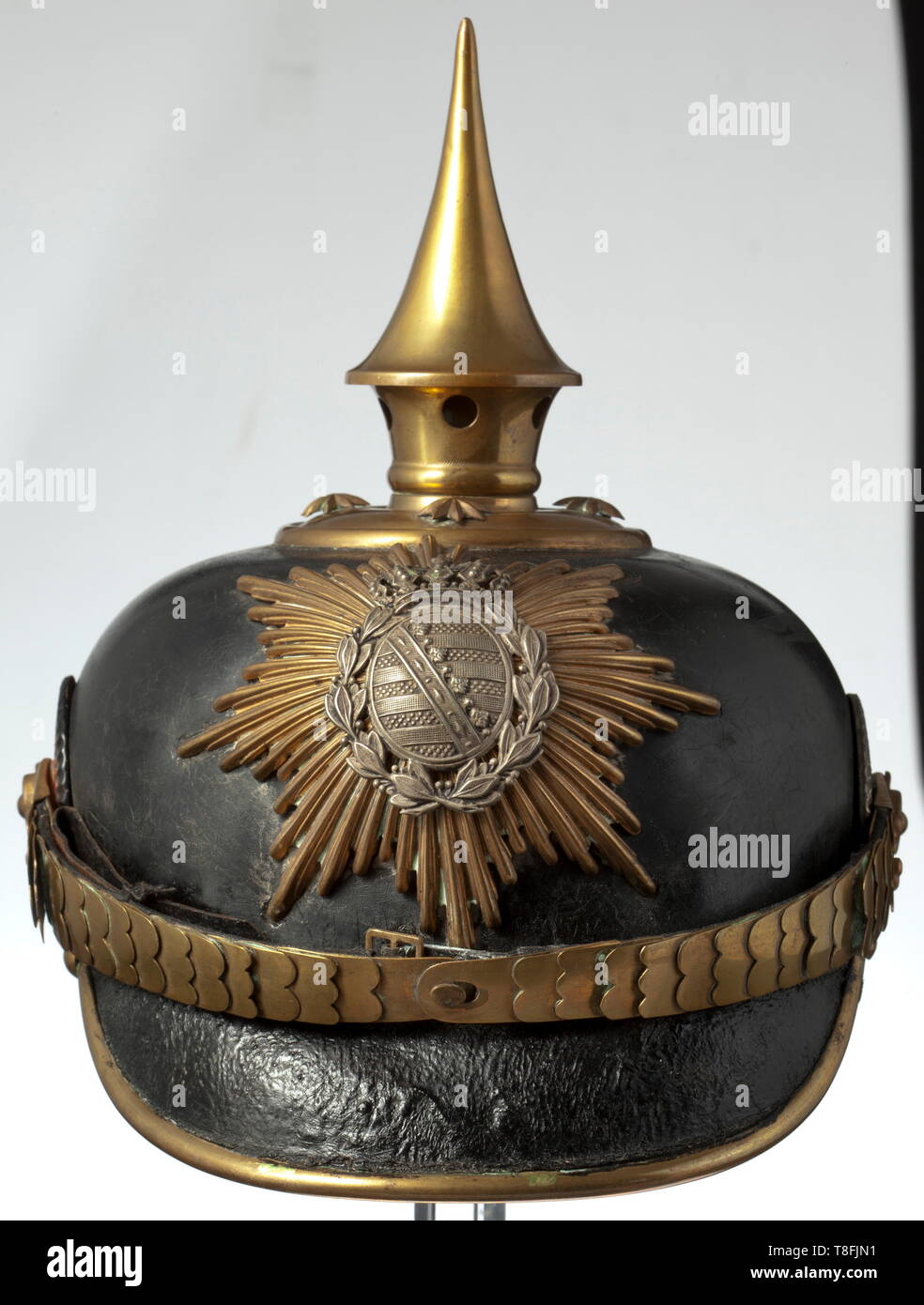 A helmet for a one-year volunteer of the infantry, circa 1900 Black painted leather skull (with craquelures) with gilt brass fittings, yellow rayed emblem with applied nickel silver coat of arms, the circular base with stars and unscrewable spike. Flat brass chinscales with leather underlay on button 91, imperial and state cockades. Brown silk rep liner and brown leather sweatband. Signs of usage and age. A beautiful, untouched piece. historic, historical, Saxony, Saxonia, Saxonian, German, Germany, 20th century, Additional-Rights-Clearance-Info-Not-Available Stock Photo