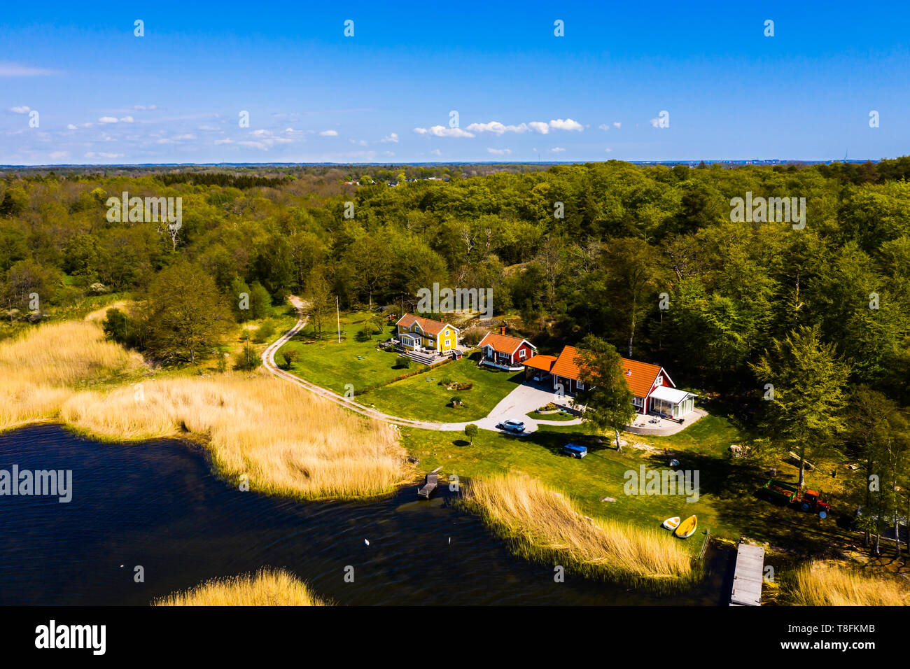 Small seaside village seen from above on a sunny spring day. Country road winding up to the houses from the forest. Sea with reed beds and private jet Stock Photo