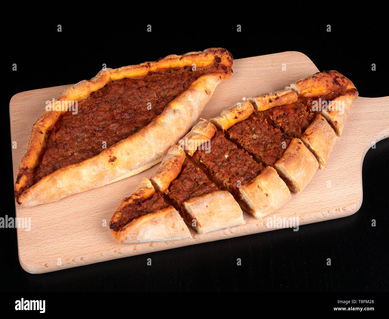 Traditional Turkish pide with beef and onions, on a wood cutting board, with dark brown background Stock Photo