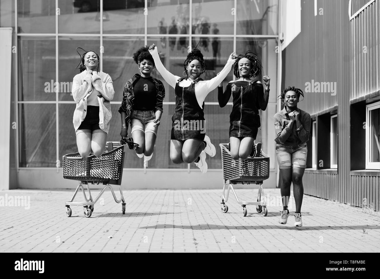 Group of five african american woman with shopping carts having fun together and jumping outdoor. Stock Photo