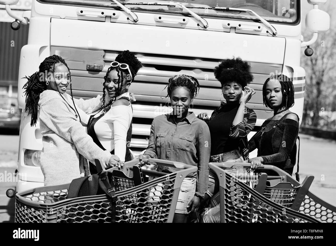 Group of five african american woman with shopping carts having fun together outdoor against truck. Stock Photo