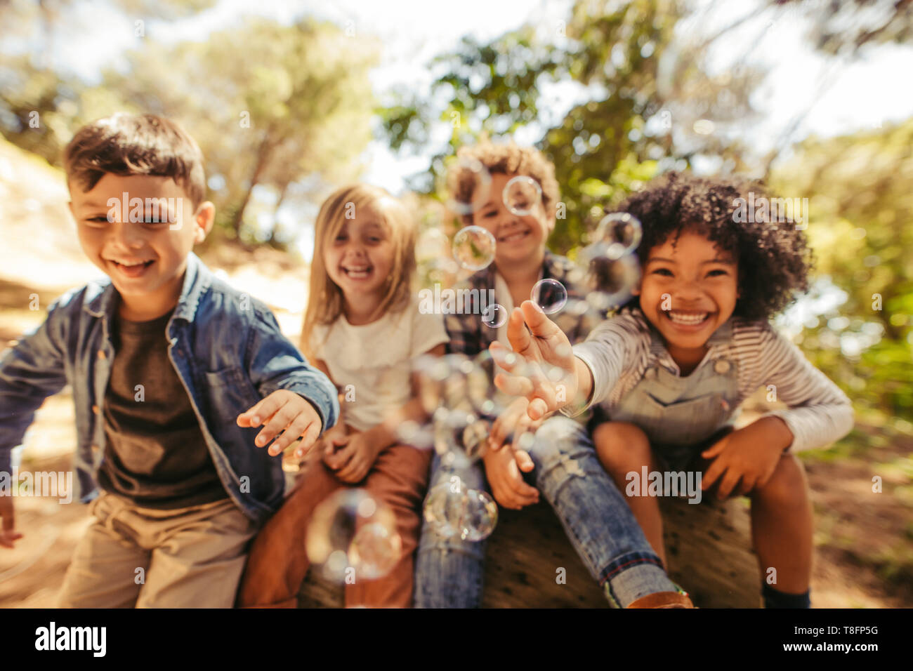 Group of children playing with soap bubbles outdoors. Friends trying to catch the bubbles. Stock Photo