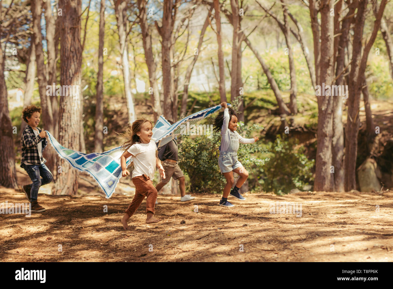Four kids running in park with picnic blanket. Group of children enjoying together in park Stock Photo