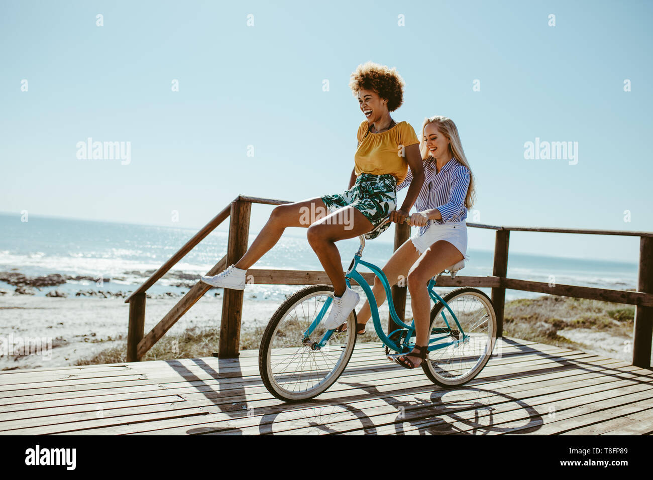 Woman riding a bicycle with her friend sitting on the handlebar. Two
