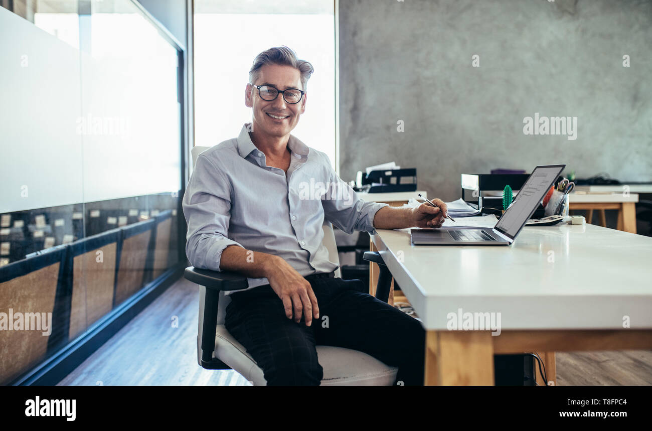 Positive mature businessman sitting at office desk. Mid adult caucasian male executive at work. Stock Photo