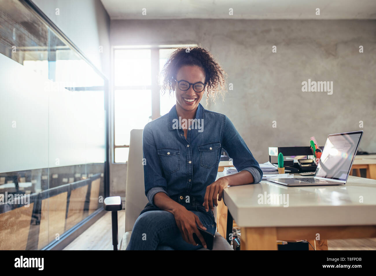Positive young businesswoman sitting at office desk. Young african female at work. Stock Photo