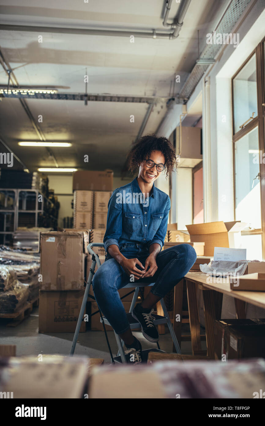 Online business owner sitting at her workdesk. Young woman with shipment boxes around looking at camera and smiling. Stock Photo