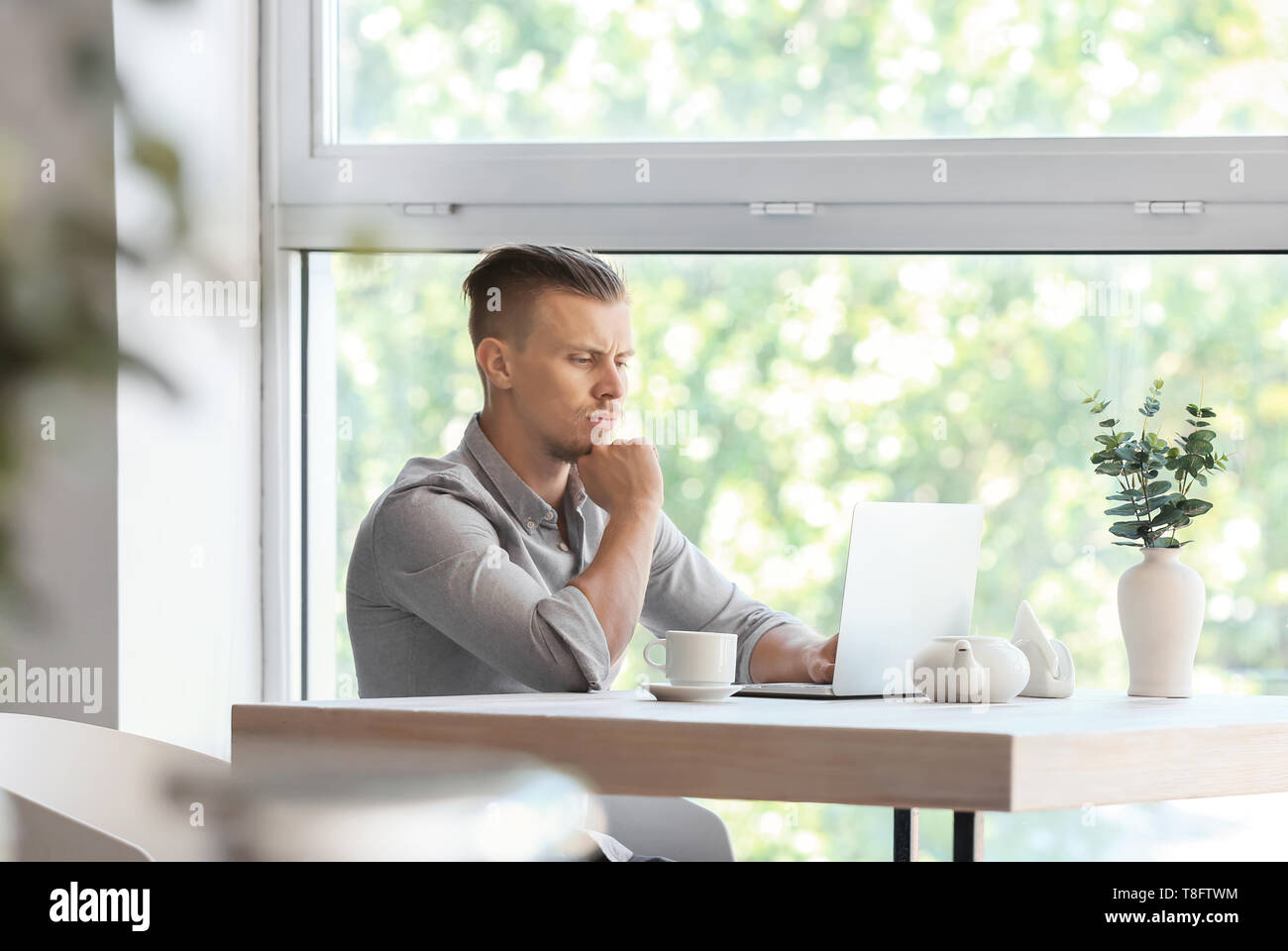 Troubled freelancer working on laptop in cafe Stock Photo