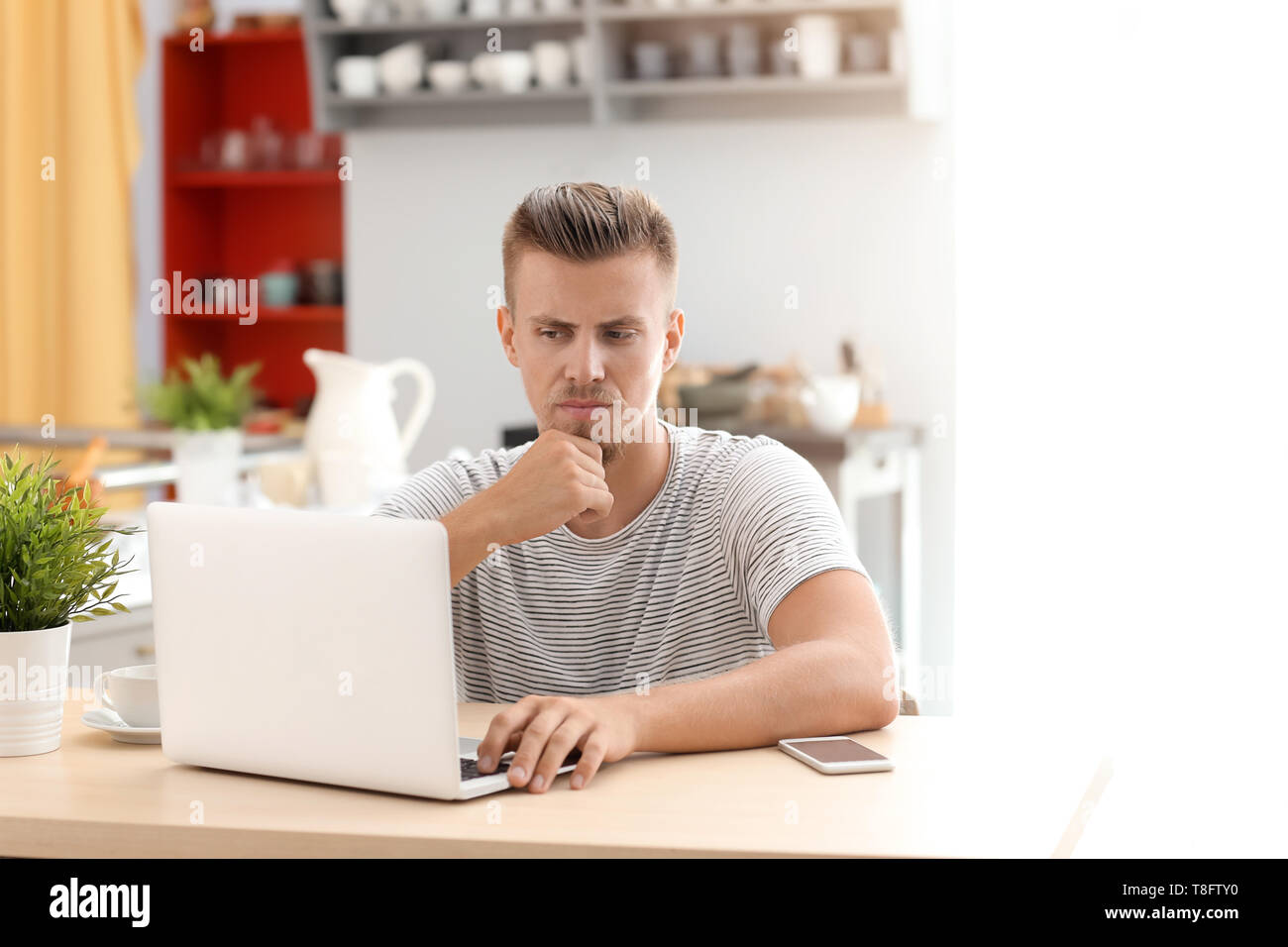 Emotional freelancer working on laptop in kitchen Stock Photo